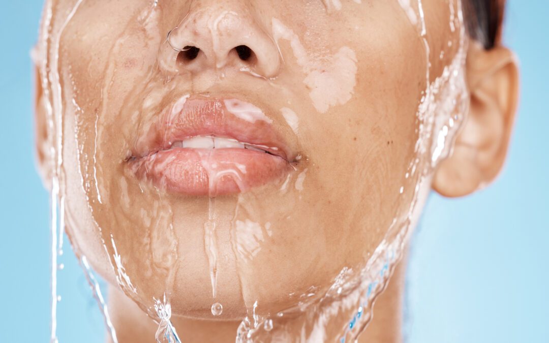 A close-up image of a person's face with water streaming down their skin, highlighting the freshness and hydration. The background is a solid light blue, emphasizing the clarity and cleanliness of the water.