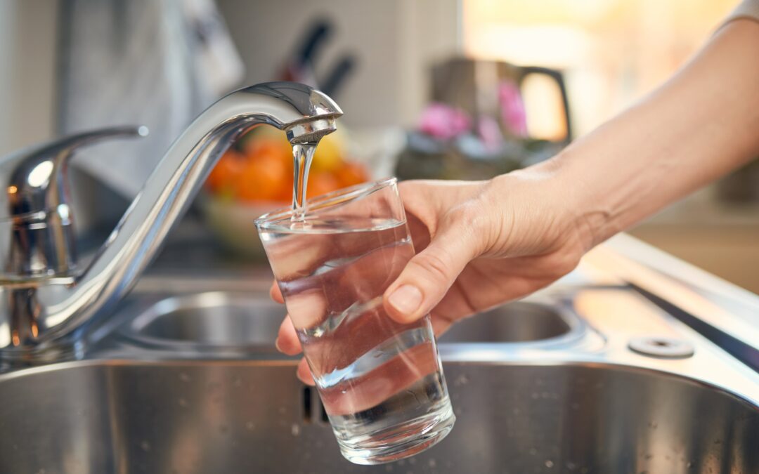 A person filling a glass of water from a kitchen faucet, representing clean and filtered water for home use.