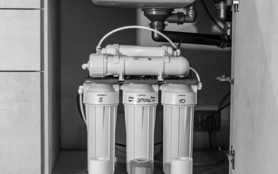 A black and white image of a water filtration system installed under a sink. The system features multiple labeled best water filters, including "Sediment 5" and "Carbon 10," with visible tubing and connectors. The setup is housed in a cabinet, showcasing its compact design and functionality.